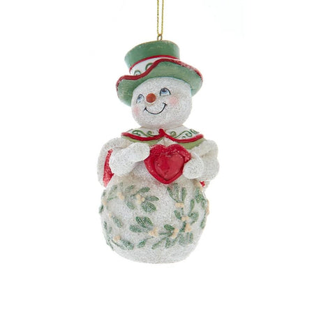 Snowman ornament with a green top hat and mistletoe detailing, holding a red heart with both hands.