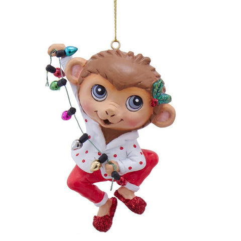 Monkey ornament in white pajamas with red dots, holding colorful Christmas string lights and wearing red glitter slippers.