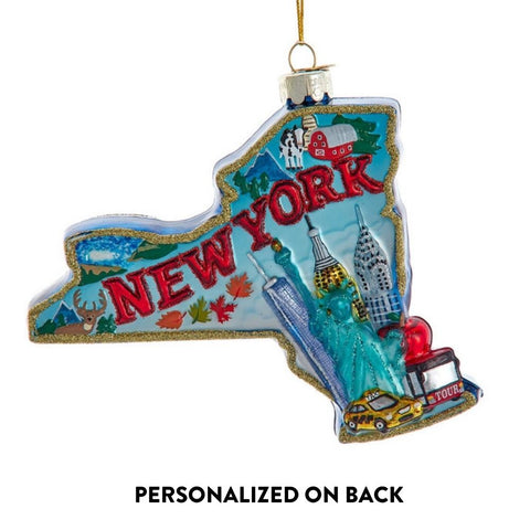 Glass ornament shaped like the state of New York with colorful cityscape artwork, New York lettering, and iconic landmarks including the Statue of Liberty and skyscrapers.