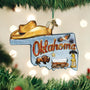 Christmas ornament shaped like the state of Oklahoma with a cowboy hat, train, and other elements on a blurred Christmas tree background.