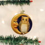 Decorative Christmas ornament with an owl and face on a crescent moon, hanging on a tree.