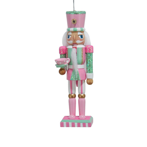 Pink and mint nutcracker ornament with glittered accents, tall hat, white beard, and pink teacup with saucer on a striped base.