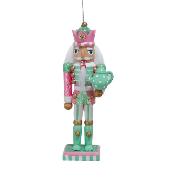 Pink and mint nutcracker ornament with glittered details, a crown-style hat, white beard, and polka dot teapot standing on a striped base.