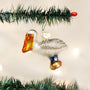 Glass pelican ornament hanging on a Christmas tree branch with lights in the background