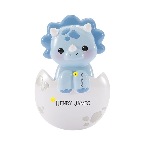 Personalized blue baby triceratops ornament in a cracked white egg with name and year placement shown.
