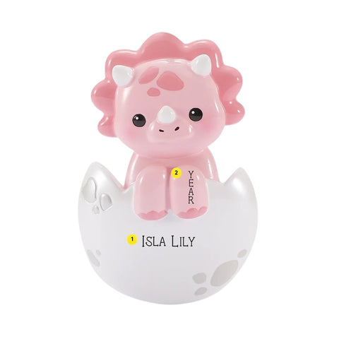 Personalized pink baby triceratops ornament in a cracked white egg with name and year placement shown.