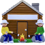 Decorative ornament of two people by a cabin with a campfire, on a white background.