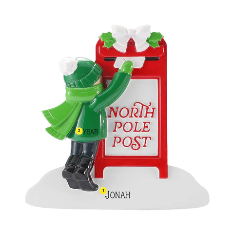 Child sending Santa a letter ornament personalized with a name on the snowy base and a year on the child’s coat beside a red North Pole post mailbox.