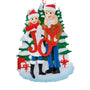 JOY couple ornament with two adults in winter clothes standing in front of snowy evergreen trees with wrapped gifts.