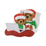 Cozy Christmas bear couple ornament with Santa hats, green pajamas, laptop, mug, pillow, and red blanket.