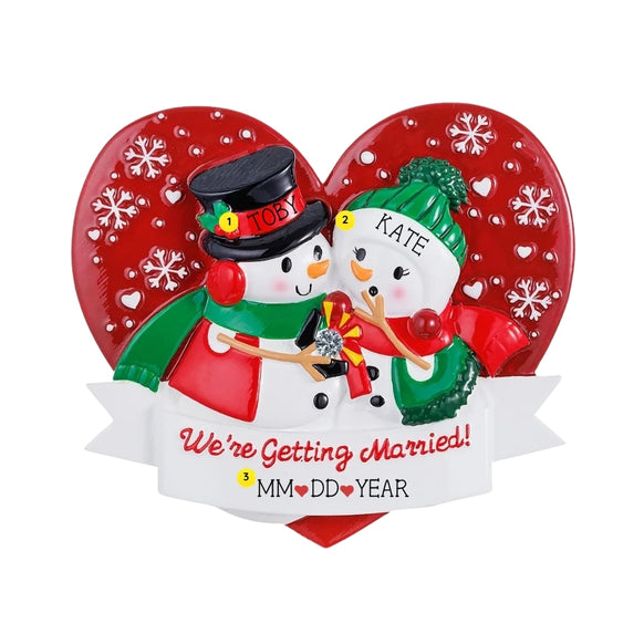 Personalized engagement snowman couple ornament with names on the hats, wedding date on the base, and “We’re Getting Married!” on the banner.