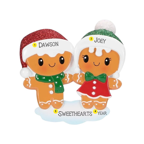 Personalized gingerbread couple ornament with names on the Santa hat brims, a phrase on the snowy base, and the year added near the bottom.