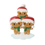 Gingerbread family of three ornament with smiling gingerbread people in Santa hats and green scarves, standing on a snowy base.