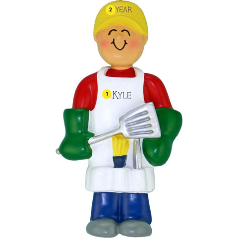 Ornament of a person in a yellow hat and red shirt holding a spatula, personalized with name and year on an apron, on a white background.