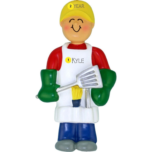 Ornament of a person in a yellow hat and red shirt holding a spatula, personalized with name and year on an apron, on a white background.