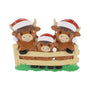 Highland cow family ornament with three cows in Santa hats standing behind a fence.