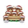 Highland cow family ornament with seven cows in Santa hats, including two little cows in buckets, gathered behind a fence.