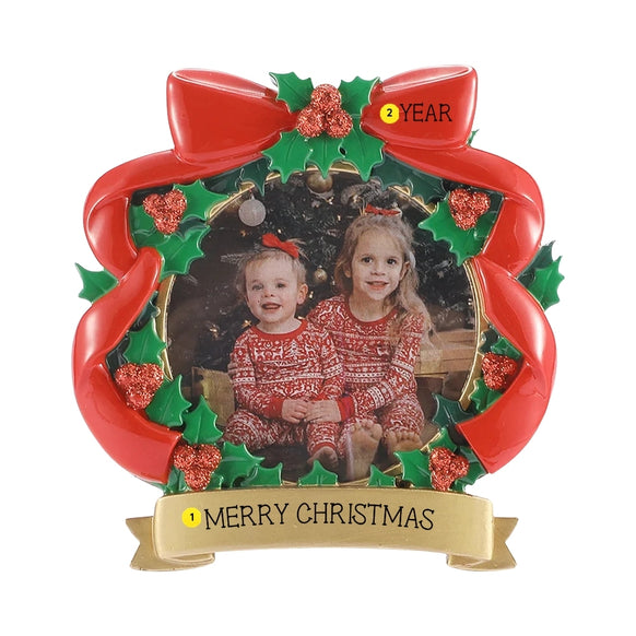 Red bow and holly Christmas picture frame ornament with a photo of two children, personalized with an example phrase on the banner and a year on the bow.