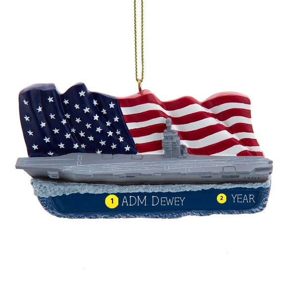 U.S. Navy™ aircraft carrier ornament with gray ship, waving American flag background, blue personalization area, and gold hanging cord.