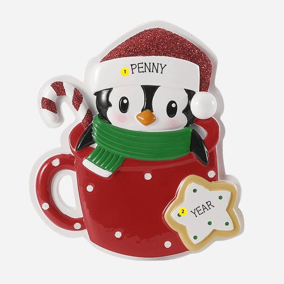 Personalized penguin in a cocoa mug ornament with a name on the Santa hat and year added to the star cookie.