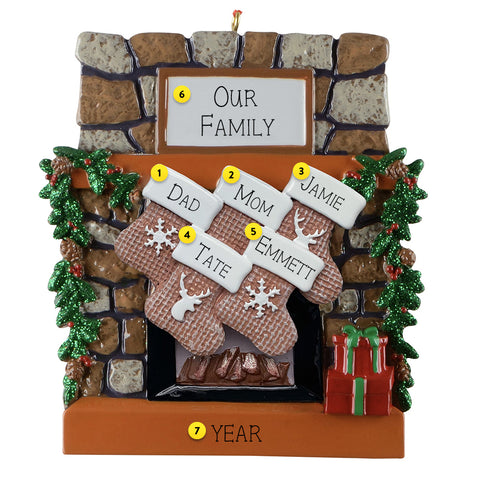 Personalized Christmas ornament with family names on stockings against a stone fireplace background.