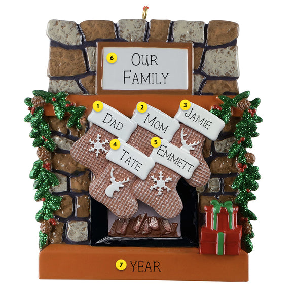 Personalized Christmas ornament with family names on stockings against a stone fireplace background.