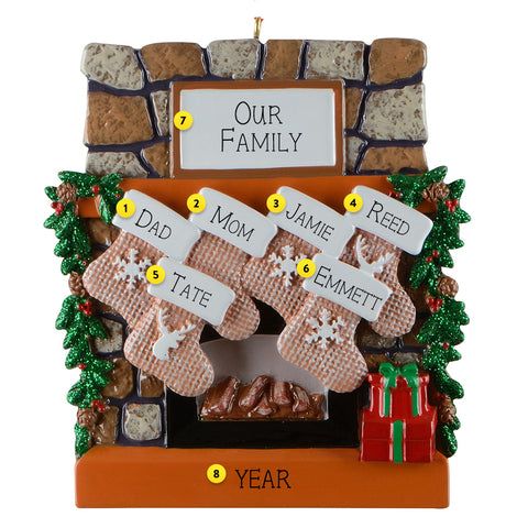 Personalized Christmas ornament with family names on stockings against a stone fireplace background.
