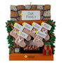 Personalized Christmas ornament with family names on stockings against a stone fireplace background.