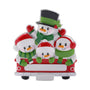 Snowman family of four ornament riding together in a red holiday truck with hats, scarves, and mittens.