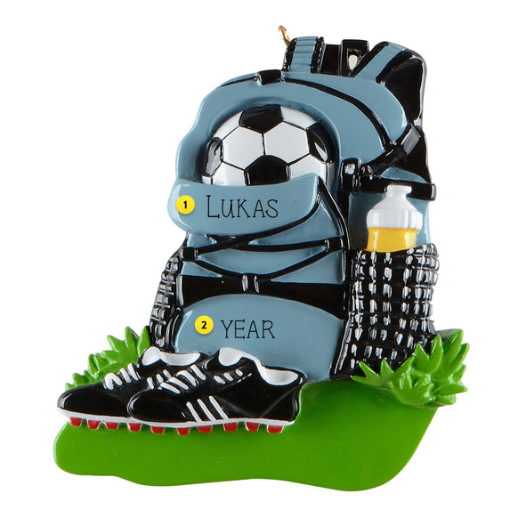 Soccer-themed ornament with backpack, soccer ball, shoes, and water bottle on a grassy base.
