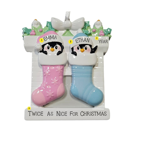 Personalized twin penguin stocking ornament with one pink stocking and one blue stocking, two baby names on the hats, a year on the mantel, and an example phrase “Twice As Nice For Christmas” on the base.