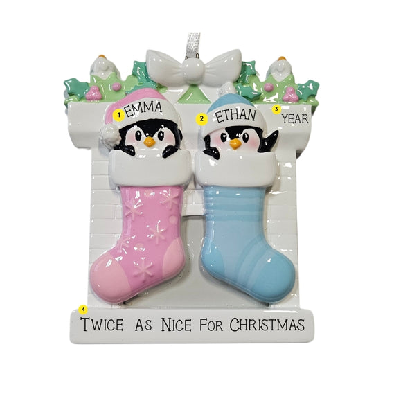 Personalized twin penguin stocking ornament with one pink stocking and one blue stocking, two baby names on the hats, a year on the mantel, and an example phrase “Twice As Nice For Christmas” on the base.