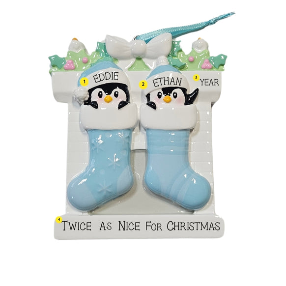 Personalized twin penguin stocking ornament with two blue stockings, two baby names on the hats, a year on the mantel, and the phrase “Twice As Nice For Christmas” on the base.