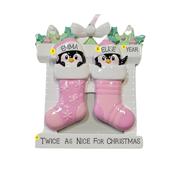 Personalized twin penguin stocking ornament with two pink stockings, two baby names on the hats, a year on the mantel, and the phrase “Twice As Nice For Christmas” on the base.