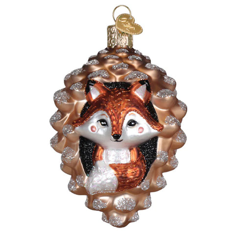 Glass ornament of a fox peeking out from a pine cone on a white background