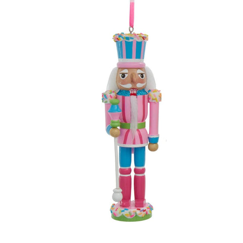 Pink and blue pastel nutcracker ornament with a sprinkle-covered hat, white beard, and candy scepter standing on a round sprinkled base.