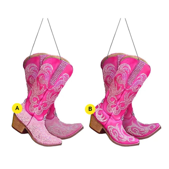 Two pink rhinestone cowboy boot ornaments with scrolling decorative details, wood-look heels, and black hanging cords.