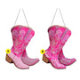 Two pink rhinestone cowboy boot ornaments with scrolling decorative details, wood-look heels, and black hanging cords.