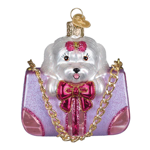 Decorative ornament of a white dog with a pink bow on a pink handbag with gold chain.