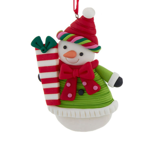 Snowman ornament in a green outfit with a red bow and striped hat, holding a red and white wrapped present.