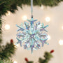 Iridescent snowflake ornament hanging on a Christmas tree with blurred lights in the background