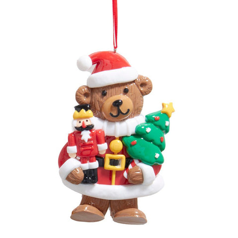 Bear ornament dressed in a red Santa coat and hat, holding a small nutcracker figure and a green Christmas tree.