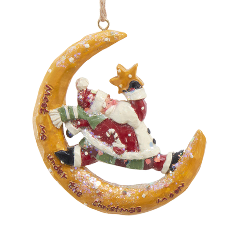 Santa resting inside a glittered golden crescent moon while holding a star ornament.