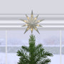 12" silver glitter star treetop lit on a Christmas tree in front of a snowy window scene.