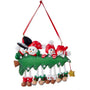 Snowman family of 4 ornament with four smiling snowmen peeking over a decorated Christmas tree with dangling legs and space for a family name or short phrase and year.