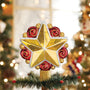 Gold and red swirly star tree topper displayed on top of a decorated Christmas tree branch with lights in the background.