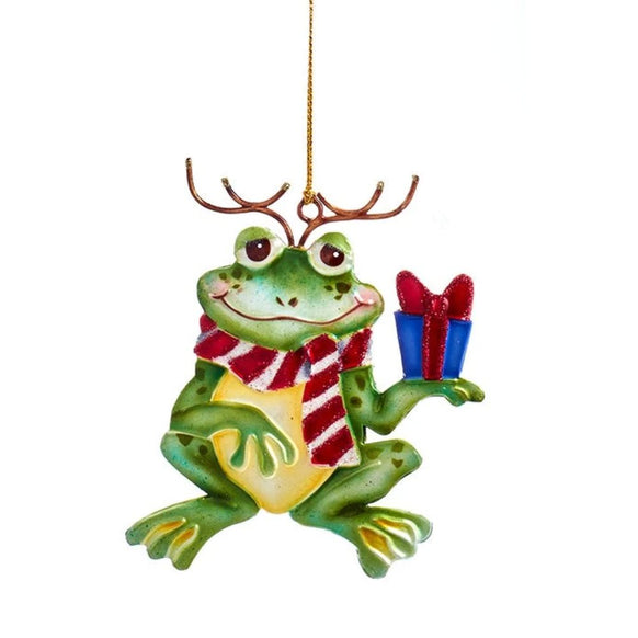 Tin Christmas frog ornament with reindeer antlers, red and white striped scarf, smiling green frog, and blue gift with red bow.