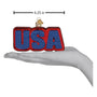 Decorative ornament with 'USA' in red and blue on a white background with a hand to show size