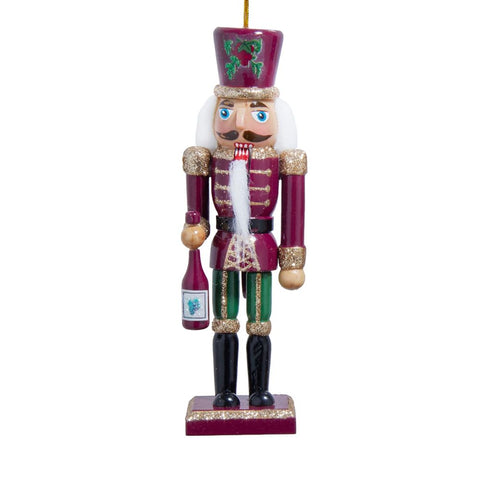 Burgundy, green, and gold nutcracker ornament with a white beard, glittered trim, and a small wine bottle in hand on a rectangular base.