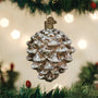 Decorative pine cone ornament hanging on a Christmas tree with lights in the background.
